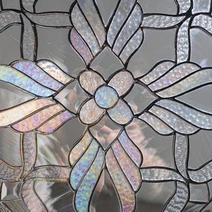 May include: A stained glass window with a geometric design featuring a flower in the center and four stylized leaves around it. The glass is iridescent and has a rainbow effect.
