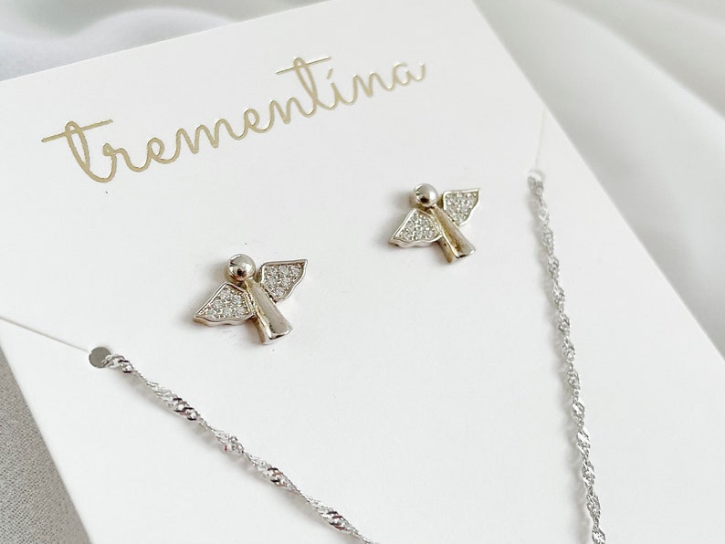 以下が含まれることがあります： 白いカードに「trementina」という文字が筆記体で書かれた、透明なクリスタルアクセントが付いたシルバーのエンジェルイヤリングのペアです。