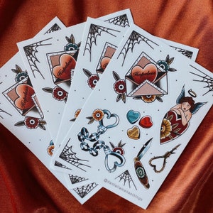 May include: A sticker sheet featuring traditional tattoo-style illustrations including an envelope with a heart labeled Hopeless, heart-shaped handcuffs, a pocket knife, a rope noose, a winged figure, spider webs, flowers, and small heart candies.