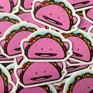 May include: A set of pink taco stickers with a cartoon face. The stickers are printed on white paper and have a glossy finish.