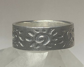 May include: A silver ring with a textured design of swirling patterns and small circles. The ring is wide and has a polished finish.