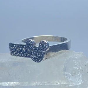 Puede incluir: Un anillo de plata con un dise&ntilde;o de marcasita negra en forma de cabeza de Mickey Mouse.
