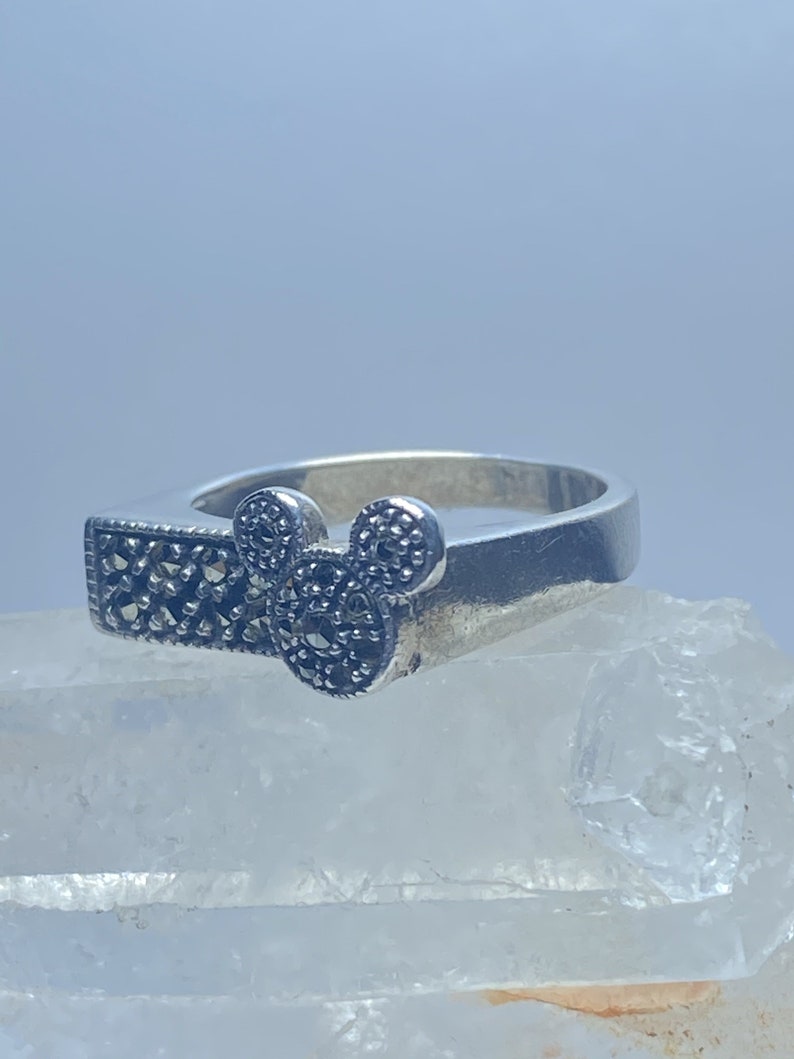 Puede incluir: Un anillo de plata con un dise&ntilde;o de marcasita negra en forma de cabeza de Mickey Mouse.