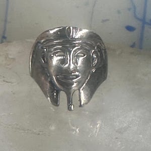 May include: A silver ring with a detailed design of a pharaoh's head.