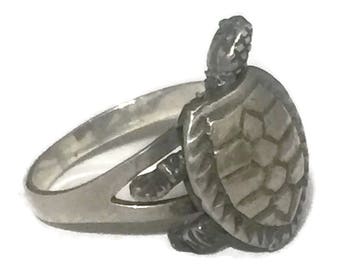 May include: A silver ring with a detailed turtle design. The turtle is facing to the right and has a textured shell.