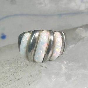 May include: A silver ring with a ribbed design, featuring alternating sections of polished silver and white opal. The opal sections have a subtle iridescent quality, reflecting various colors. The ring has a rounded shape.