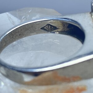 Puede incluir: Primer plano del interior de un anillo de plata con la inscripci&oacute;n "21" dentro de un rombo.