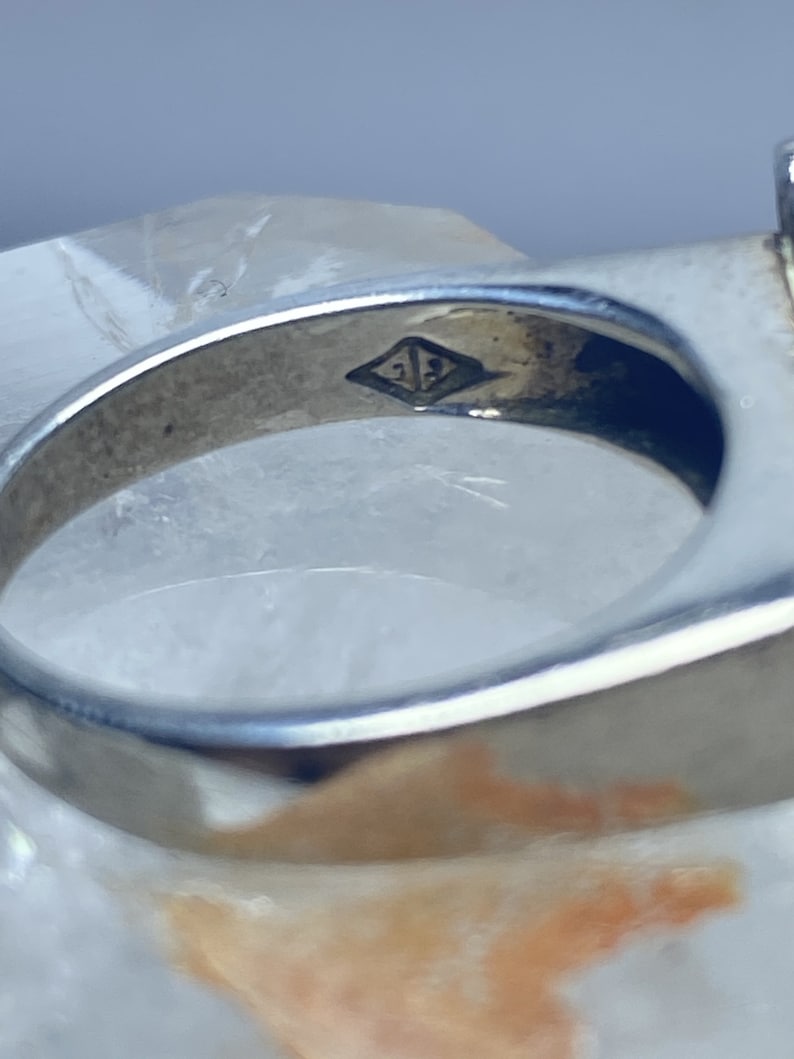 Puede incluir: Primer plano del interior de un anillo de plata con la inscripci&oacute;n "21" dentro de un rombo.