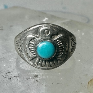 Op de afbeelding: Een zilveren ring met een turquoise steen in het midden. De ring heeft een ingewikkeld ontwerp van een vogel met uitgespreide vleugels.