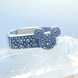Puede incluir: Un anillo de plata con un dise&ntilde;o de cabeza de Mickey Mouse en marcasita negra. El anillo est&aacute; sobre un fondo blanco.