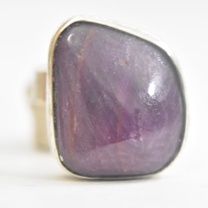 May include: A silver ring with a large, purple, irregularly shaped gemstone.