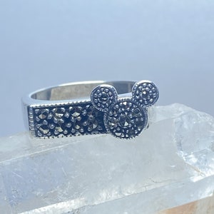 Puede incluir: Un anillo de plata con un dise&ntilde;o de cabeza de Mickey Mouse hecho de piedras de marcasita negras.