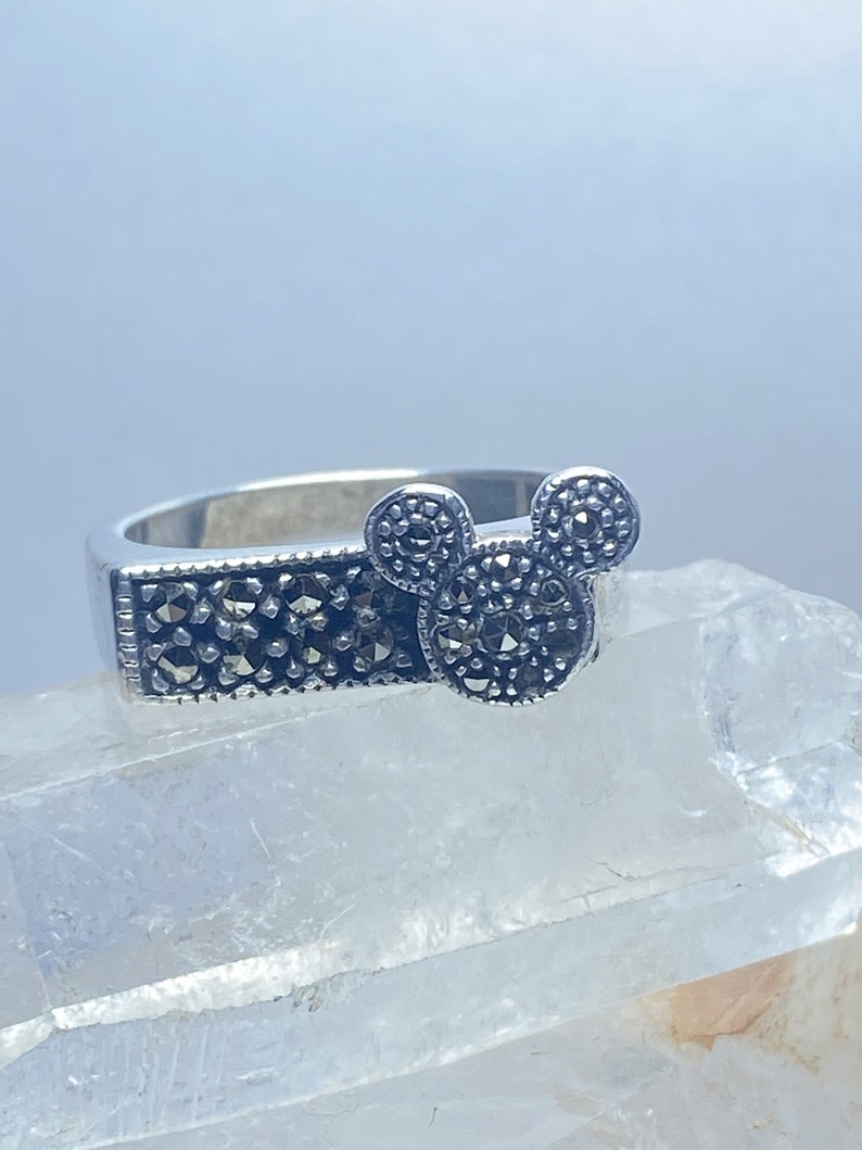 Puede incluir: Un anillo de plata con un dise&ntilde;o de cabeza de Mickey Mouse hecho de piedras de marcasita negras.