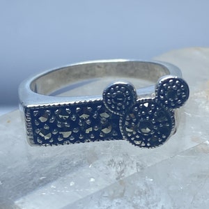 Puede incluir: Un anillo de plata con un dise&ntilde;o de Mickey Mouse en negro y plata. El anillo est&aacute; engastado con piedras de marcasita negras.
