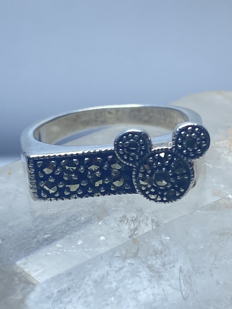 Puede incluir: Un anillo de plata con un dise&ntilde;o de Mickey Mouse en negro y plata. El anillo est&aacute; engastado con piedras de marcasita negras.