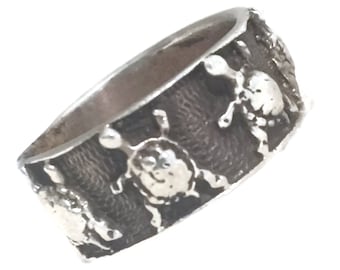 May include: A silver ring with a textured band and a design of multiple turtles around the band.