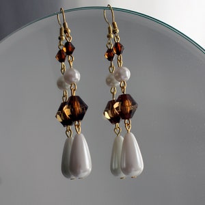 Puede incluir: Pendientes colgantes con ganchos y cadenas doradas. Cuentan con cuentas facetadas marrones, cuentas blancas con forma de perla y colgantes en forma de lágrima. Un accesorio sofisticado. Una adición elegante.