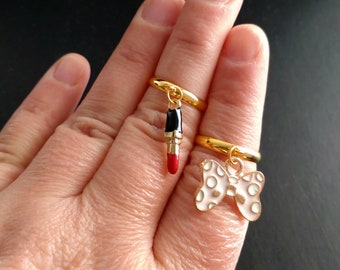 Anelli con ciondoli color oro. Anelli regolabili per tutte le taglie. Anelli con ciondoli. Due anelli tra cui scegliere. Ciondoli a forma di rossetto o fiocco. Regalo per lei. Anello pendente