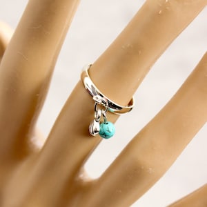 May include: A silver ring with a turquoise stone and a silver charm hanging from it.
