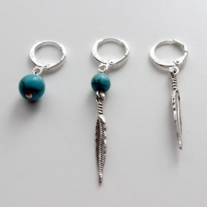 May include: Three silver hoop earrings with turquoise accents. The earrings on the left and center have a turquoise bead, while the earring on the right has a turquoise feather charm.