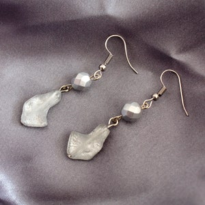 May include: A pair of silver earrings with a teardrop-shaped glass charm and a silver bead on each earring.