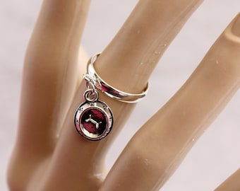 May include: A silver ring with a charm that features the Gemini zodiac symbol. The ring is on a model's finger.