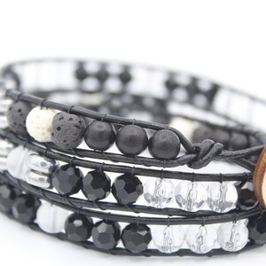 May include: A black leather wrap bracelet with black, white and silver beads. The bracelet has a wooden button closure.