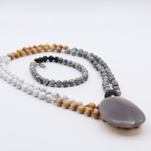 May include: A layered necklace with a large grey agate pendant. The necklace is made of white, grey, and brown beads.