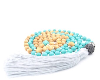 May include: A turquoise and natural wood beaded necklace with a gray tassel. The necklace is made of round beads and has a lava stone bead at the end.