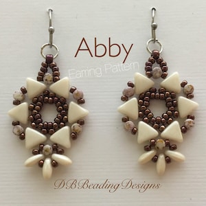 Puede incluir: Un par de pendientes de cuentas blancas y marrones con un diseño geométrico. Los pendientes se llaman "Abby" y son un patrón de abalorios.
