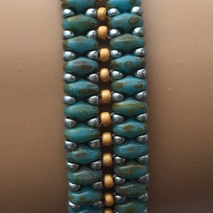May include: A turquoise and gold beaded bracelet with a silver accent. The bracelet is made with small, round beads and is worn on a person's wrist.