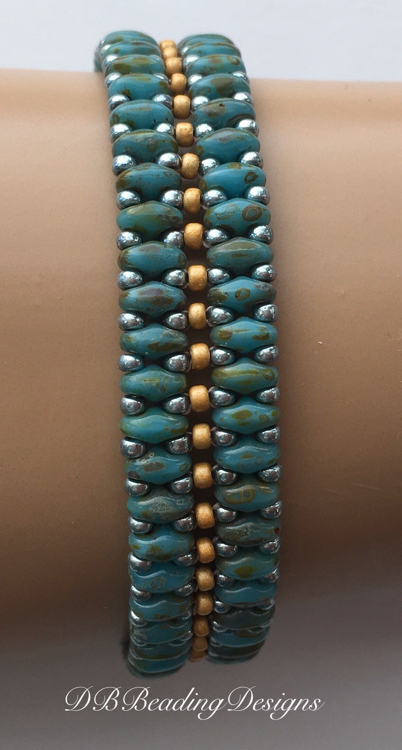 May include: A turquoise and gold beaded bracelet with a silver accent. The bracelet is made with small, round beads and is worn on a person's wrist.