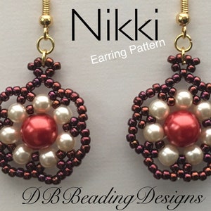 May include: Close-up of two beaded earrings. Each earring features a central red bead surrounded by white beads and a circular frame of dark red beads. The earrings are suspended from gold-colored hooks. Text on the image reads "Nikki Earring Pattern" and "DB Beading Designs."