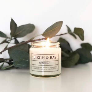 May include: A white soy massage candle in a glass jar with a black label that reads "&bull;BIRCH & BAY. SENSUAL HAND POURED SOY MASSAGE CANDLE WITH A THERAPEUTIC BLEND OF ESSENTIAL OILS"