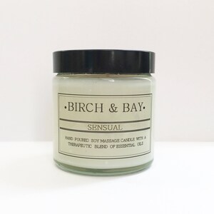 May include: A glass jar candle with a black lid. The label reads "&bull;BIRCH & BAY. SENSUAL HAND POURED SOY MASSAGE CANDLE WITH A THERAPEUTIC BLEND OF ESSENTIAL OILS"