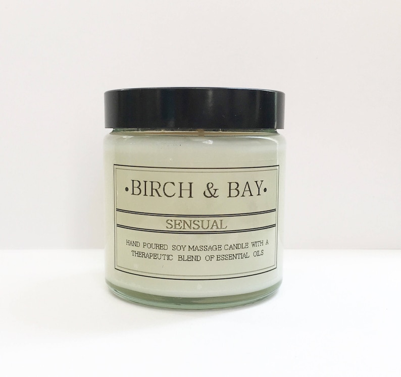 May include: A glass jar candle with a black lid. The label reads "&bull;BIRCH & BAY. SENSUAL HAND POURED SOY MASSAGE CANDLE WITH A THERAPEUTIC BLEND OF ESSENTIAL OILS"