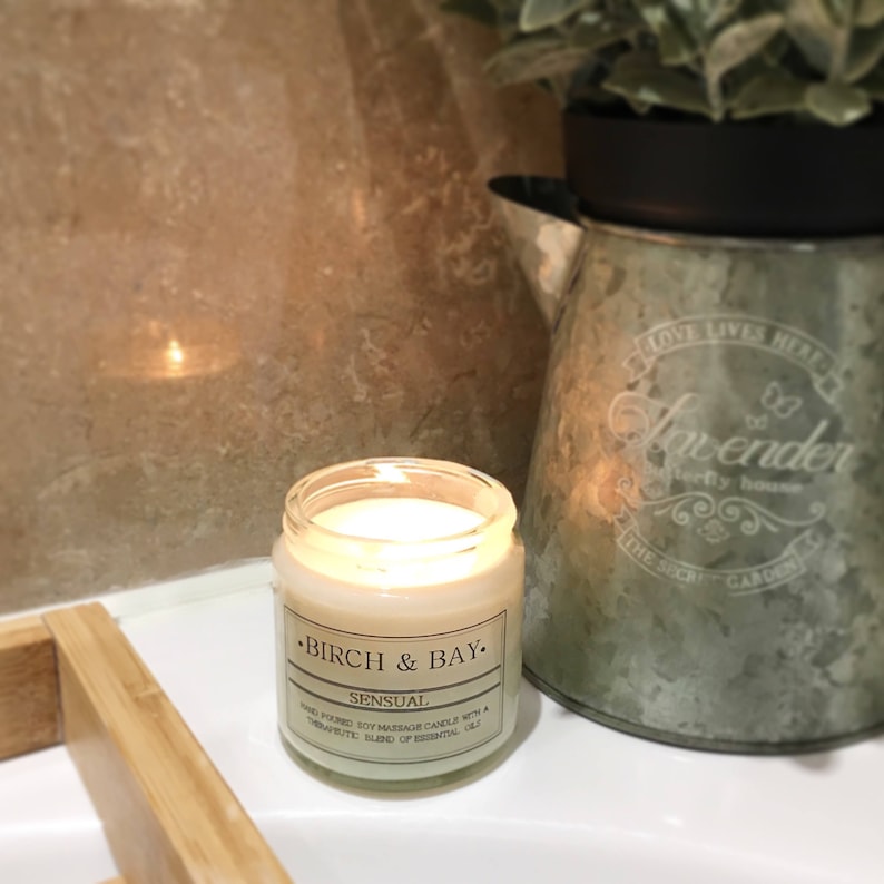 May include: A glass jar candle with a white label that reads "&bull;BIRCH & BAY. SENSUAL HAND-POURED SOY MASSAGE CANDLE WITH A THERAPEUTIC BLEND OF ESSENTIAL OILS."