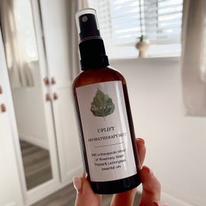May include: A brown glass bottle with a black spray nozzle and a white label. The label has a green leaf design and the text "BIRCH & BAY", "UPLIFT", "AROMATHERAPY MIST", "With a therapeutic blend of Rosemary, Black Pepper & Lemongrass essential oils".