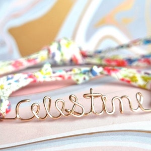 May include: A gold wire bracelet with the name "Celestine" spelled out in wire. The bracelet is on a white fabric background with a floral pattern.