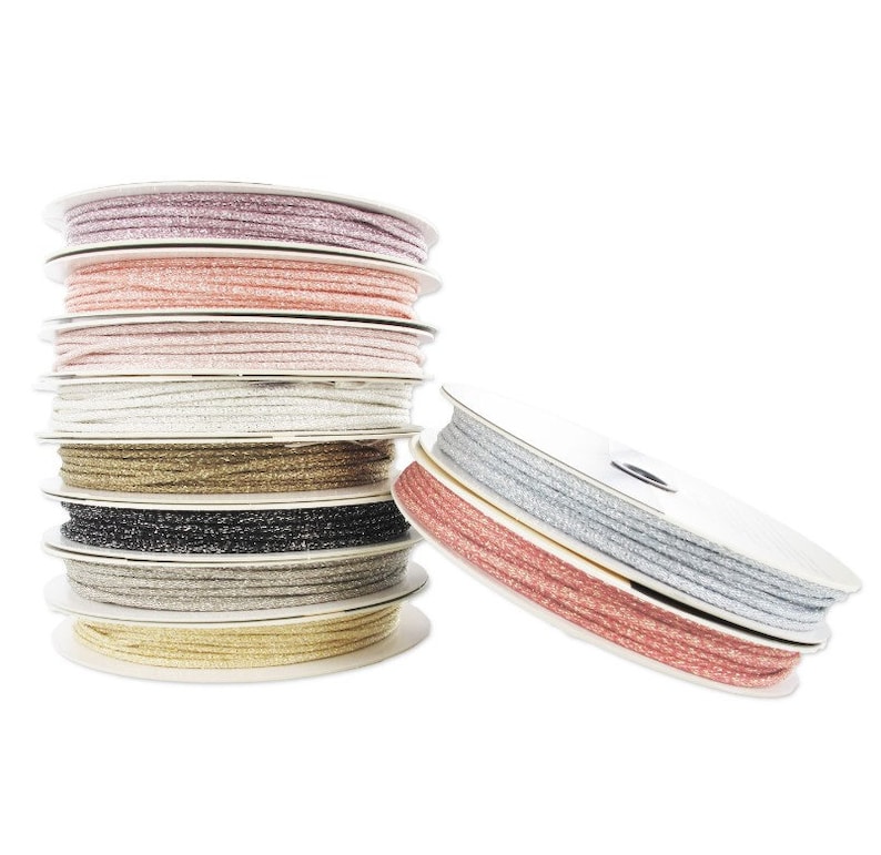 May include: A stack of spools of sparkly cord in various colors, including pink, gold, silver, and black. The cord is wound around white spools.