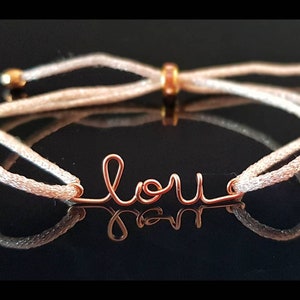 May include: A white string bracelet with a gold-colored wire charm that says "love".