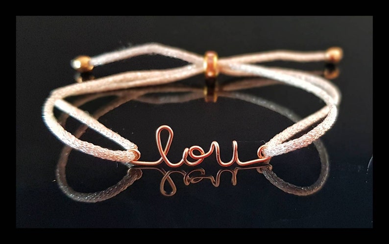 May include: A white string bracelet with a gold-colored wire charm that says "love".