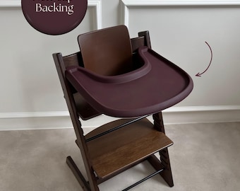 May include: A dark brown wooden high chair featuring a deep burgundy plastic tray and a matching backrest. The tray is marked with a curved arrow and a circular graphic containing the text Non-Slip Backing in white lettering.