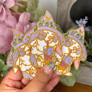 May include: Three embroidered iron-on patches featuring cartoon bunnies wearing purple and blue wizard hats and holding cups of boba tea.