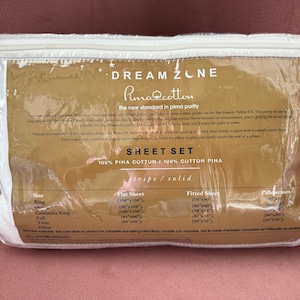 Puede incluir: Un juego de sábanas empaquetado con el texto "DREAM ZONE Pima Cotton" visible. El embalaje es transparente, mostrando un juego de sábanas blancas. También es visible el texto "SHEET SET 100% PIMA COTTON". El paquete está sellado con una cremallera blanca.