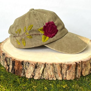 May include: A khaki baseball cap with an embroidered red rose and green leaves.