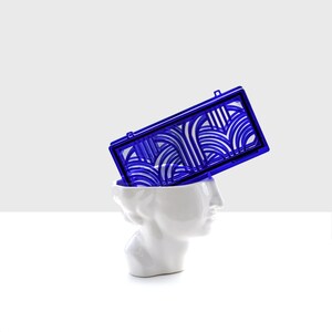 May include: A white ceramic bust with a blue geometric design on top. The design is reminiscent of an art deco style.