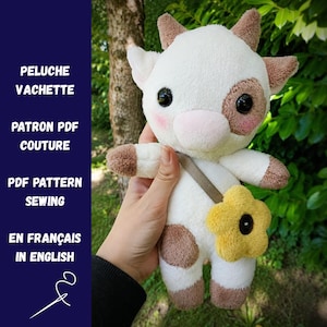 Könnte beinhalten: Ein Plüschkuh-Spielzeug mit weißem Fell, braunen Flecken und kleinen Hörnern. Es hat große schwarze Augen, rosa Wangen und eine gelbe blumenförmige Tasche mit einem dunklen Zentrum. Der Text links lautet PELUCHE VACHETTE, PATRON PDF COUTURE, PDF PATTERN SEWING, EN FRANÇAIS, IN ENGLISH.