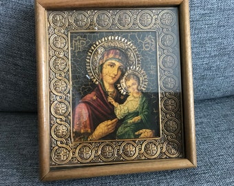 May include: A framed religious icon depicting the Virgin Mary holding a baby Jesus. The icon is set against a dark background with a gold ornate frame.
