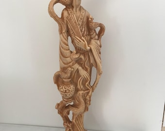 May include: A cream-colored ceramic figurine of a woman in a traditional Chinese dress holding a bird. The woman is smiling and has a delicate, intricate design. The figurine is standing on a base with a decorative design.